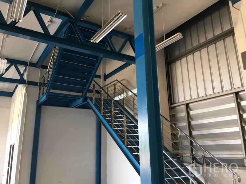 Warehouse for rent in Lat Krabang, Bangkok - Interior mezzanine area with blue steel staircase and fluorescent lighting inside the industrial warehouse.