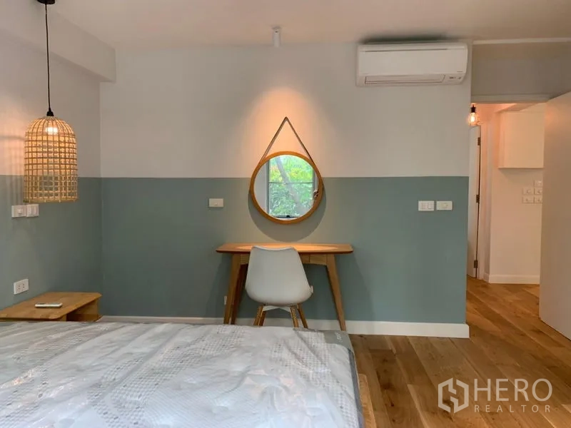 Condominium for sale in Watthana, Bangkok - Bedroom study nook with wooden desk, round mirror and air conditioner.