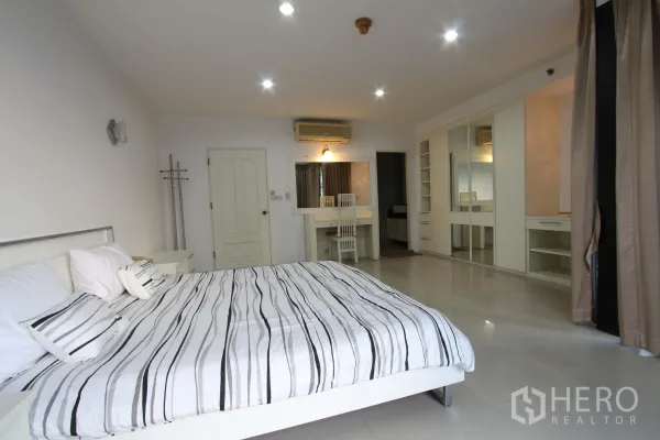 公寓 出租在Watthana, Bangkok - 宽敞主卧，条纹床品、整墙衣柜、梳妆台与筒灯照明。
