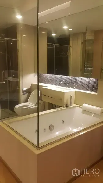 公寓 出租在Ratchathewi, Bangkok - 现代浴室，玻璃围合的浸泡浴缸、盥洗台和马桶，灯光柔和。