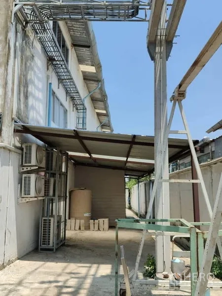 Factory for sale in Sai Noi, Nonthaburi - Covered service walkway with AC compressors and utilities along the building.