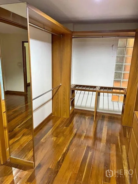 Townhouse for sale in Phra Khanong, Bangkok - Walk-in closet featuring built-in wooden wardrobes, a full-height mirror, and hardwood floors.