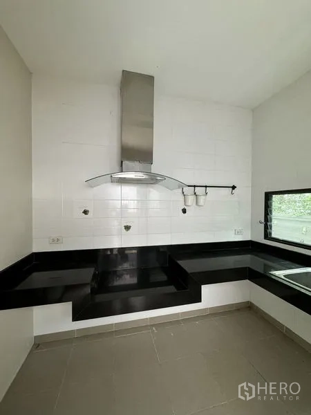 Detached House for rent in Samut Prakan - Separate Thai kitchen with black countertops, cooker hood and window.
