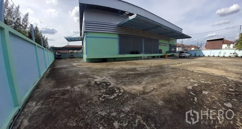 Warehouse for sale in Mueang Nonthaburi, Nonthaburi - Wide view of the fenced concrete yard surrounding the green warehouse.