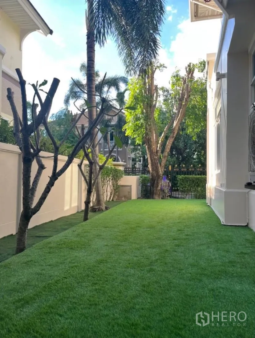 Detached House for rent or sale in Lat Phrao, Bangkok - Side yard with lush green lawn and palm trees along the house.