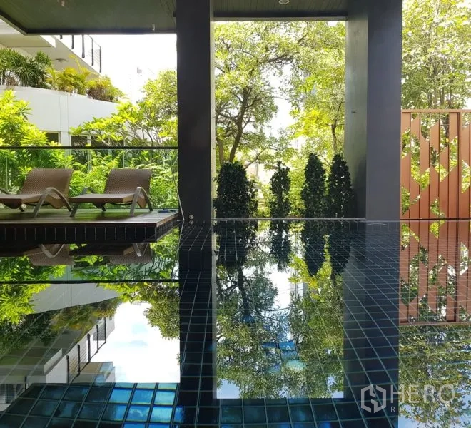 公寓 出租或出售在Watthana, Bangkok - 公寓泳池铺深色瓷砖，设躺椅，周围绿意盎然。