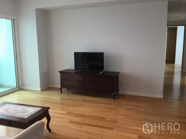 Condominium for rent in Khlong Toei, Bangkok - TV console in a spacious lounge with sliding door to the balcony and light hardwood flooring.
