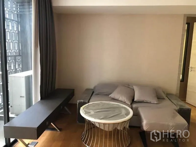 公寓 出租在Pathum Wan, Bangkok - 客厅配灰色沙发、圆形茶几与落地窗帘，采光充足。