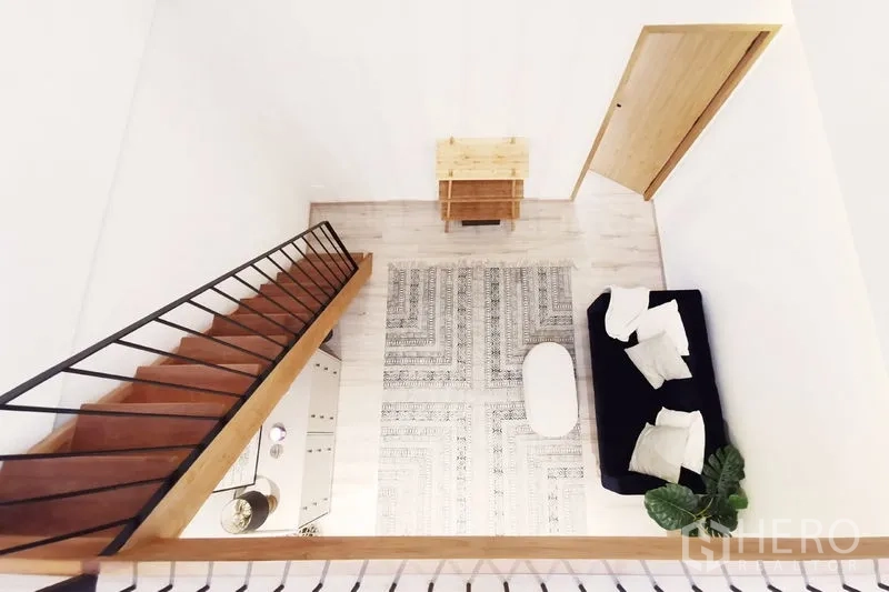 Townhouse for rent in Khlong Toei, Bangkok - Top-down view of mezzanine living area showing sofa, patterned rug and stairs.