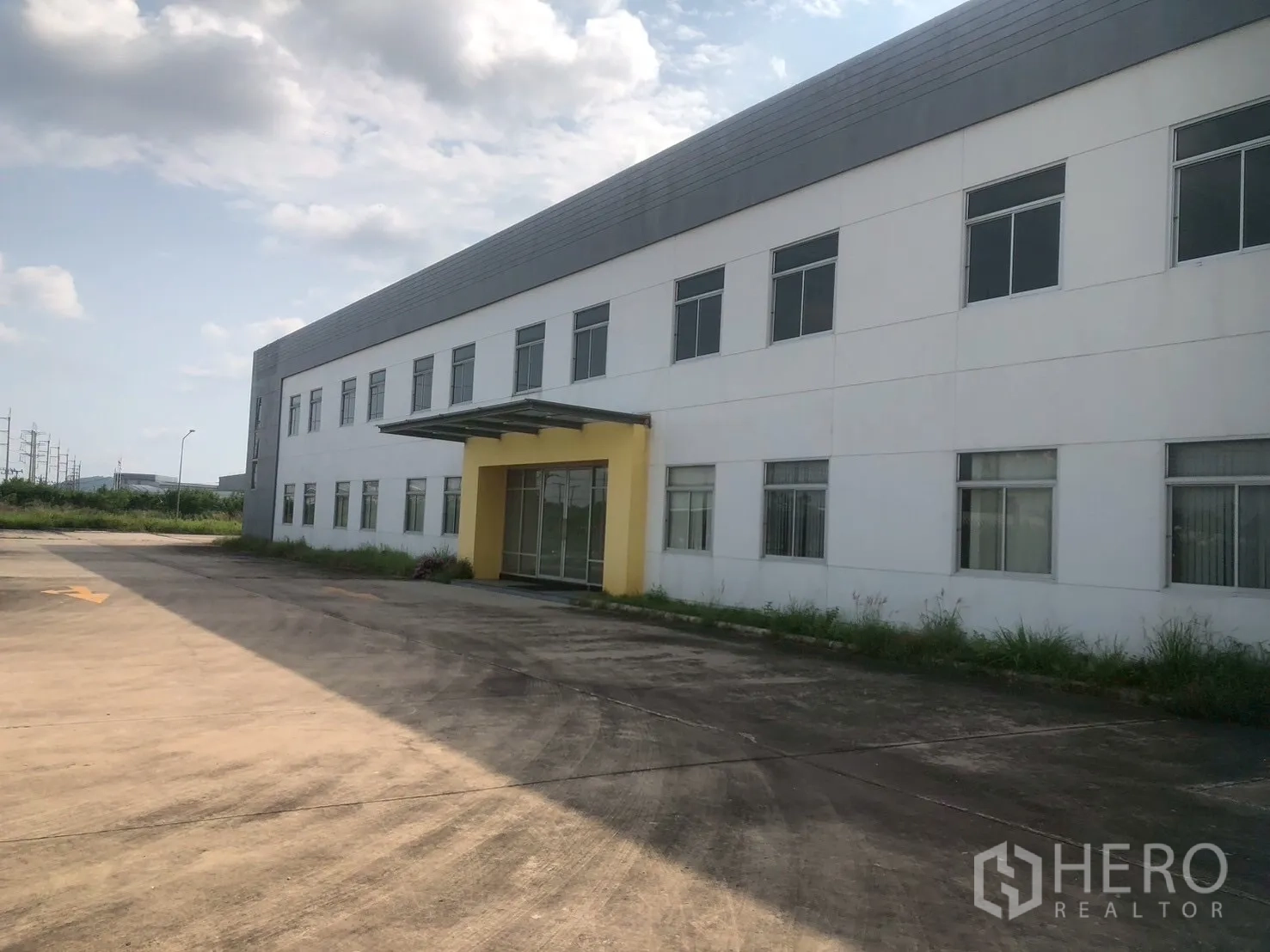 Factory for rent in Pluak Daeng, Rayong - Close exterior of the factory facade showing many windows and a glass entry under a yellow canopy.