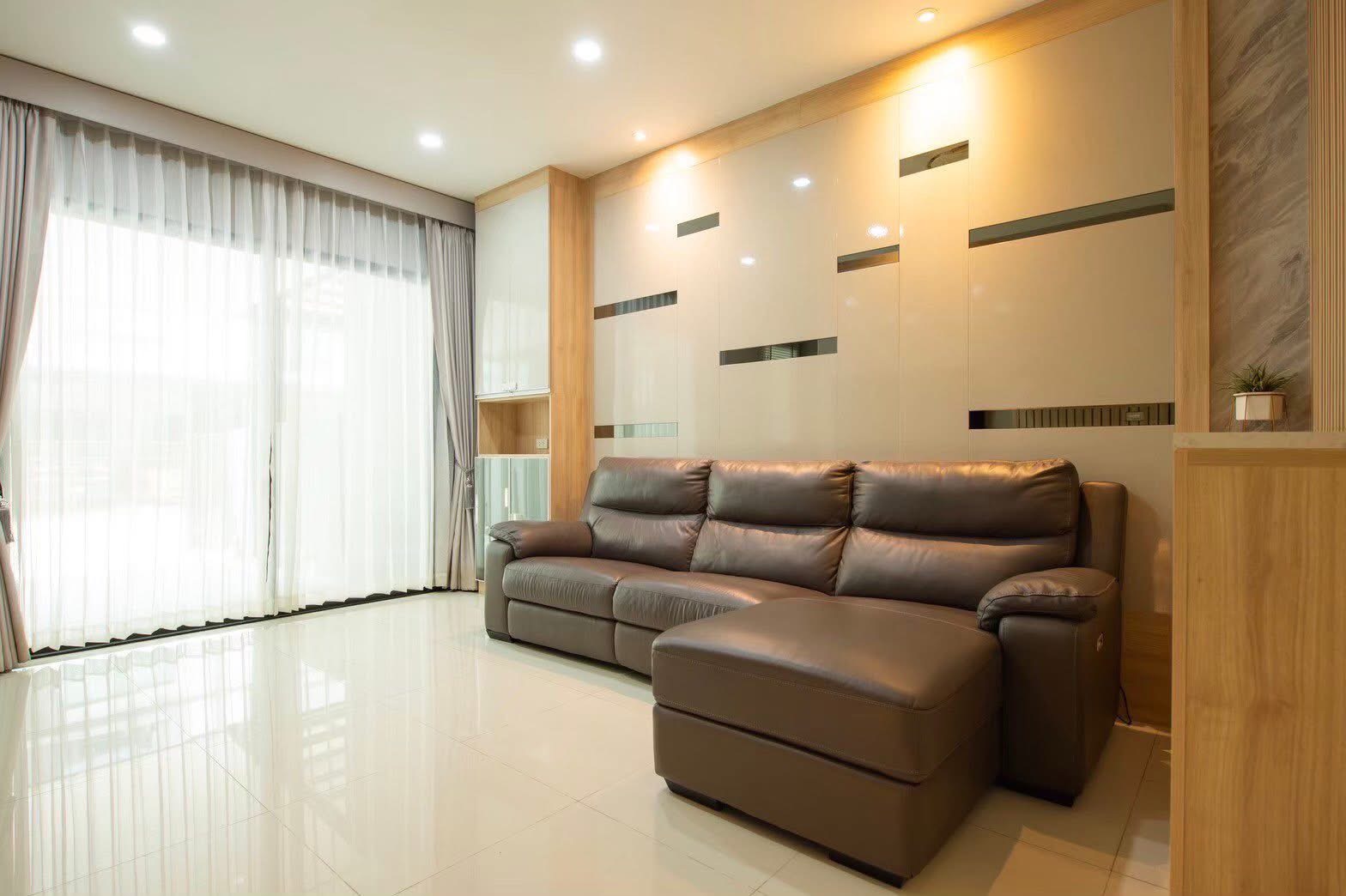 Townhouse for rent or sale in Lat Phrao, Bangkok - Spacious living room with a large leather sofa, glossy feature wall and floor-to-ceiling curtains.