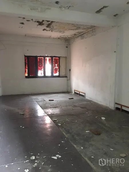 Shophouse for rent in Khlong Toei, Bangkok - Large upper-floor room needing renovation with peeling ceiling and tinted windows.