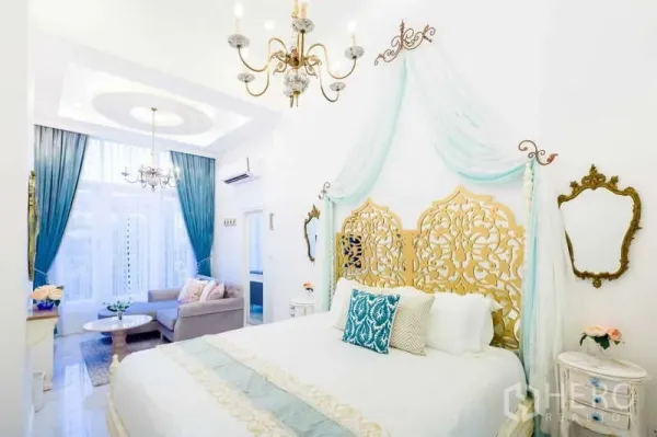 Townhouse for rent in Lat Phrao, Bangkok - Master bedroom with ornate gold headboard, canopy drapes, chandeliers and a sitting area by tall windows.