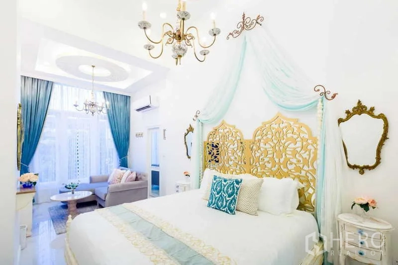 Townhouse for rent in Lat Phrao, Bangkok - Master bedroom with ornate gold headboard, canopy drapes, chandeliers and a sitting area by tall windows.
