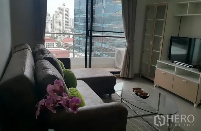 公寓 出租在Watthana, Bangkok - 沙发休闲区面向电视，旁有大滑窗与城市景色。