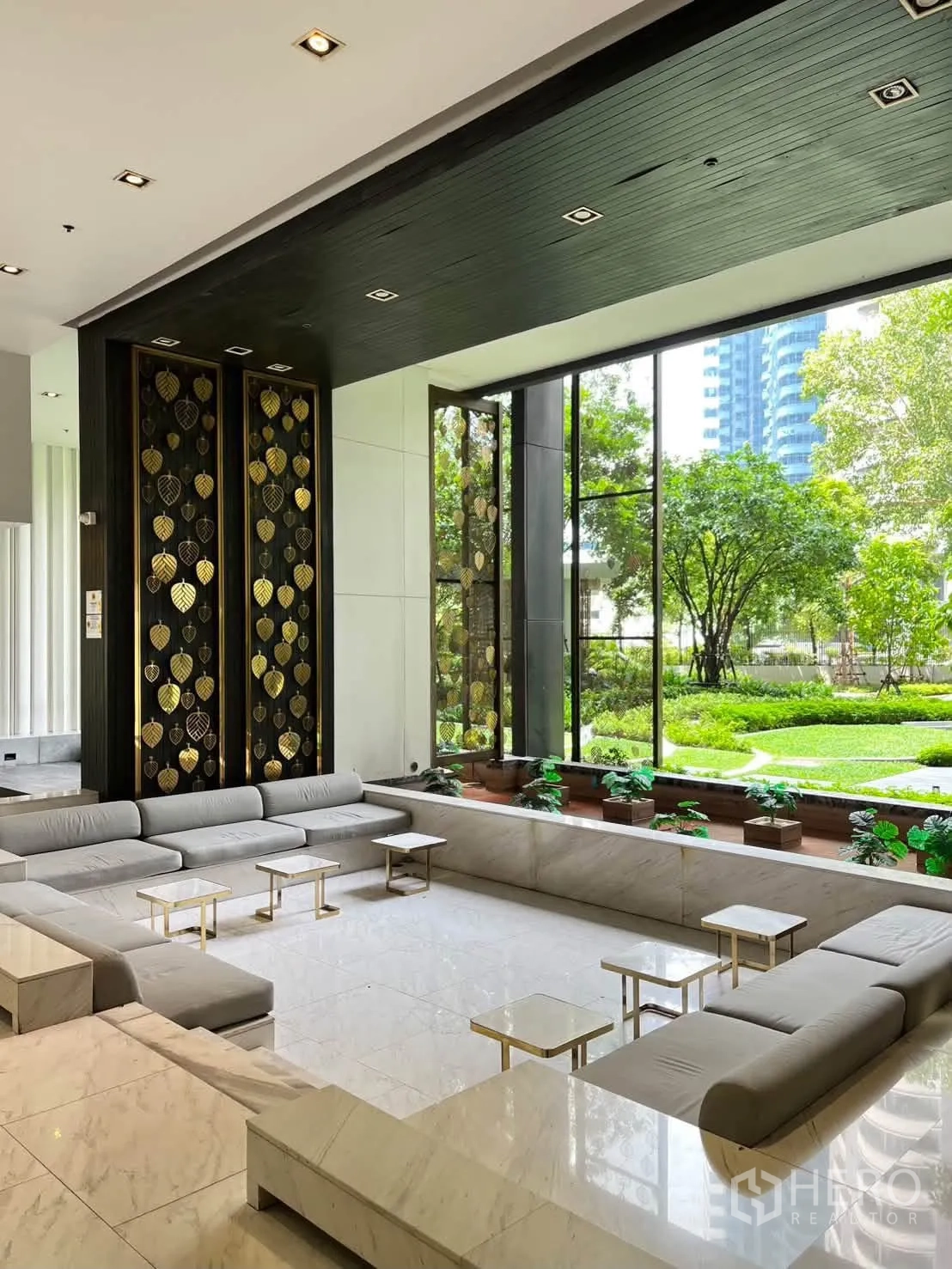 Condominium for rent in Pathum Wan, Bangkok - Elegant lobby with sunken grey sofas, marble floors, and garden view through tall windows.