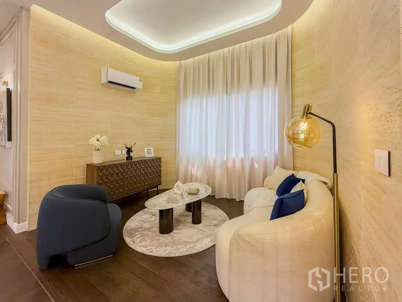 Detached House for rent or sale in Bang Kapi, Bangkok - Cozy sitting area with curved sofa, armchair, round coffee tables and soft ambient lighting.