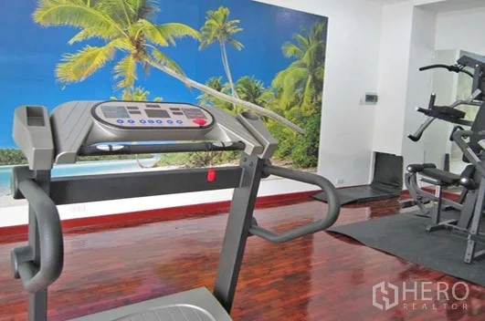 Apartment for rent in Khlong Toei, Bangkok - Fitness room with treadmill, weight machines and tropical mural on polished wooden floor