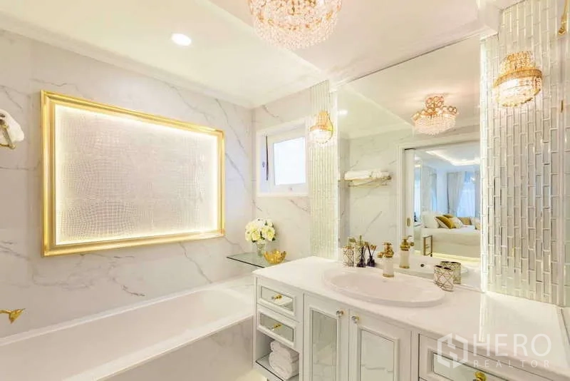 Townhouse for rent in Lat Phrao, Bangkok - Elegant white bathroom with built-in bathtub, marble walls and gold framed lighting.