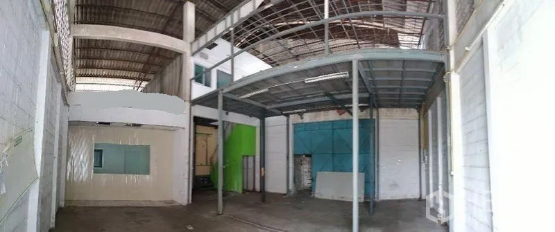 Warehouse for rent in Mueang Nonthaburi, Nonthaburi - Open warehouse interior featuring a steel mezzanine, concrete floor, small office room and large blue loading doors.