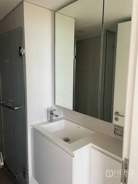 Condominium for rent in Khlong Toei, Bangkok - Modern bathroom with mirrored cabinet, square basin and glass-enclosed shower.