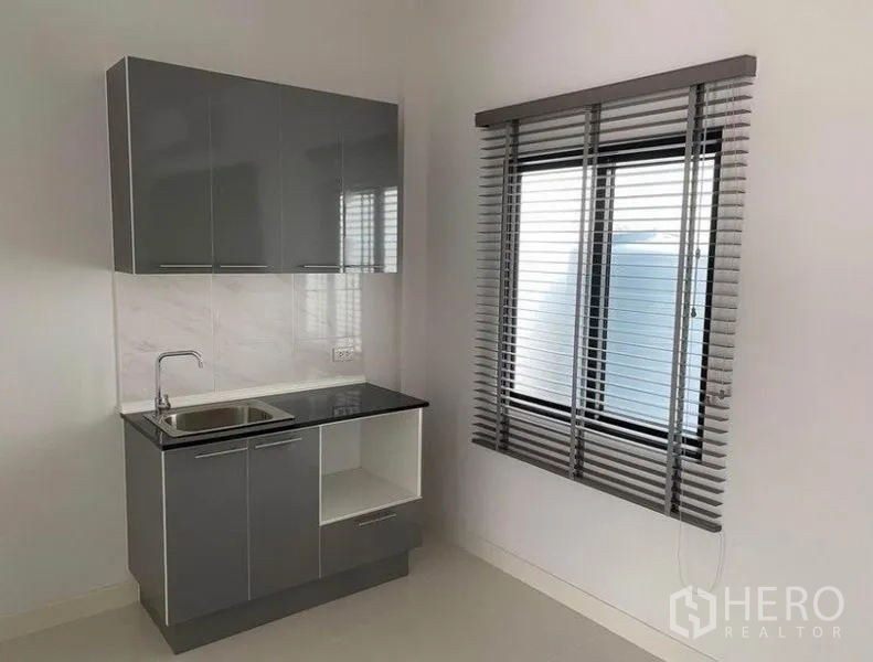 Townhouse for rent in Bang Na, Bangkok - Compact modern kitchenette with grey cabinets, stainless sink and a window with blinds.
