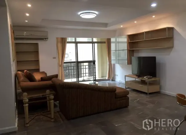 公寓 出租或出售在Watthana, Bangkok - 宽敞客厅设L形沙发、电视柜与壁挂置物架，推拉玻璃门通向阳台。