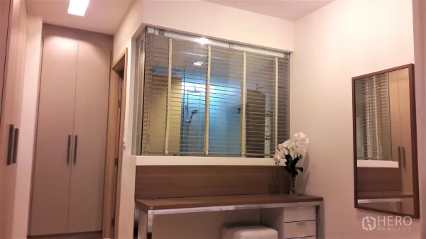 Condominium for rent in Khlong Toei, Bangkok - Dressing area with built-in wardrobes, wooden vanity and a glass partition with blinds looking into the shower.