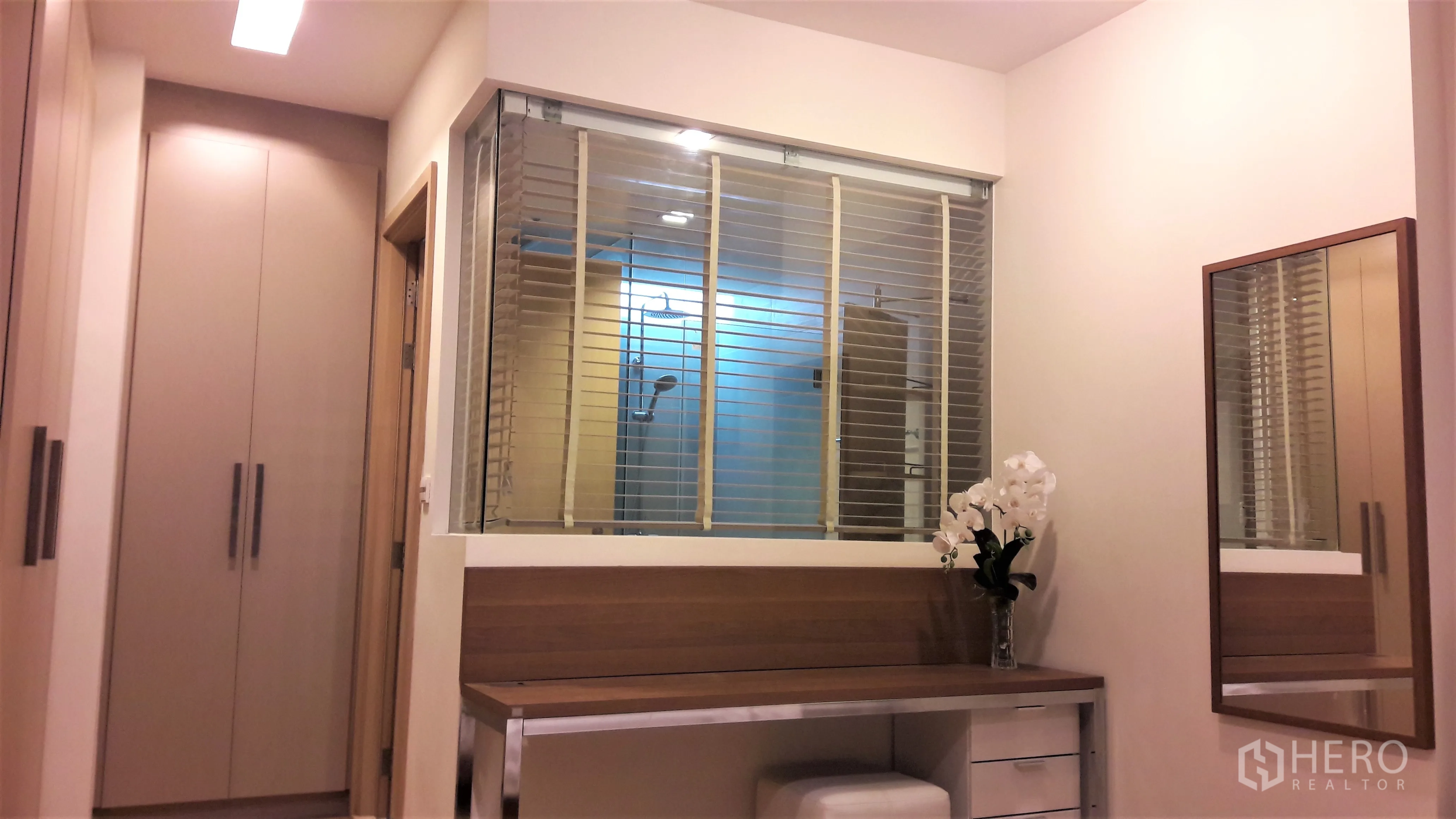 Condominium for rent in Khlong Toei, Bangkok - Dressing area with built-in wardrobes, wooden vanity and a glass partition with blinds looking into the shower.