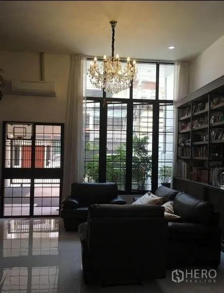 联排别墅 出租在Bang Rak, Bangkok - 挑高客厅配水晶吊灯、落地窗、皮沙发与整墙书柜。