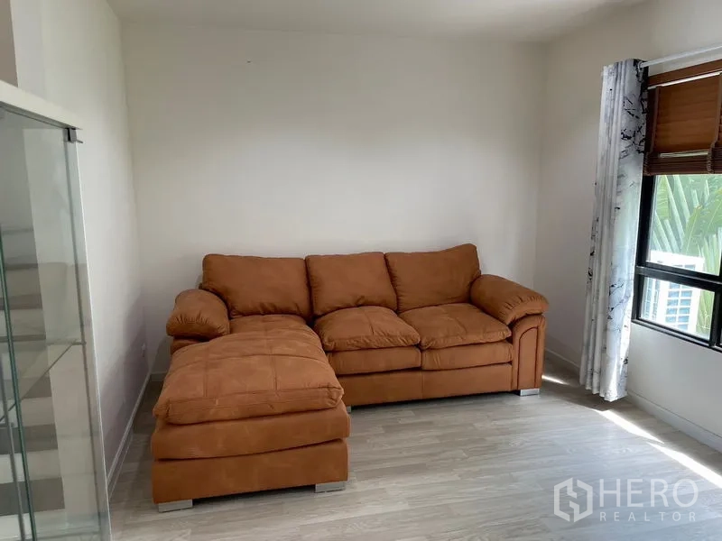 Townhouse for rent in Bang Kapi, Bangkok - Corner lounge with brown L-shaped sofa beside windows and blinds.