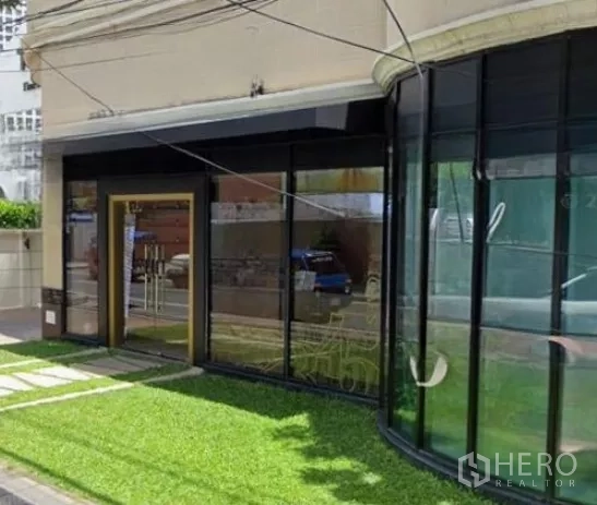零售空间 出租在Watthana, Bangkok - 入口与弧形展示玻璃的特写，旁有绿化草地