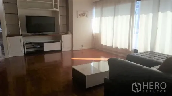 公寓 出租在Watthana, Bangkok - 采光良好的客厅，L形沙发、矮茶几与透光窗帘。