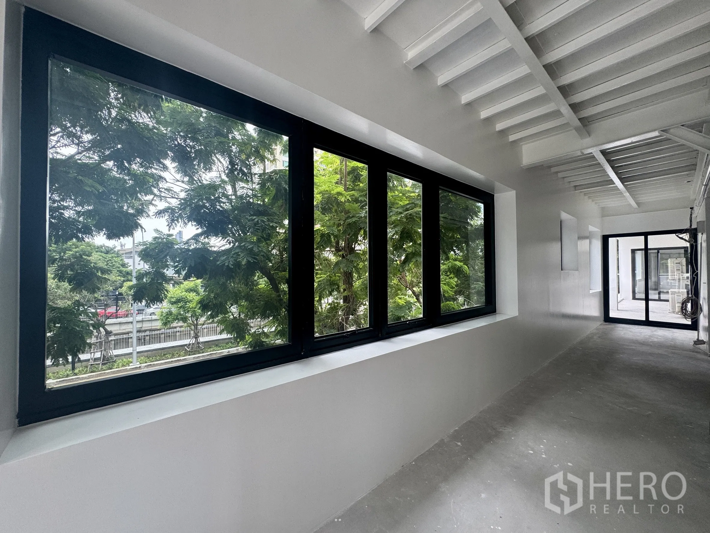 办公空间 出租在Sathon, Bangkok - 走廊设大幅黑框窗户，窗外绿意与城市道路。