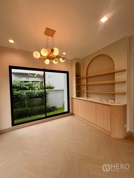 Detached House for sale in Bang Kruai, Nonthaburi - Cozy corner with built-in wooden shelves, pendant chandelier and a sliding door opening to the private garden.