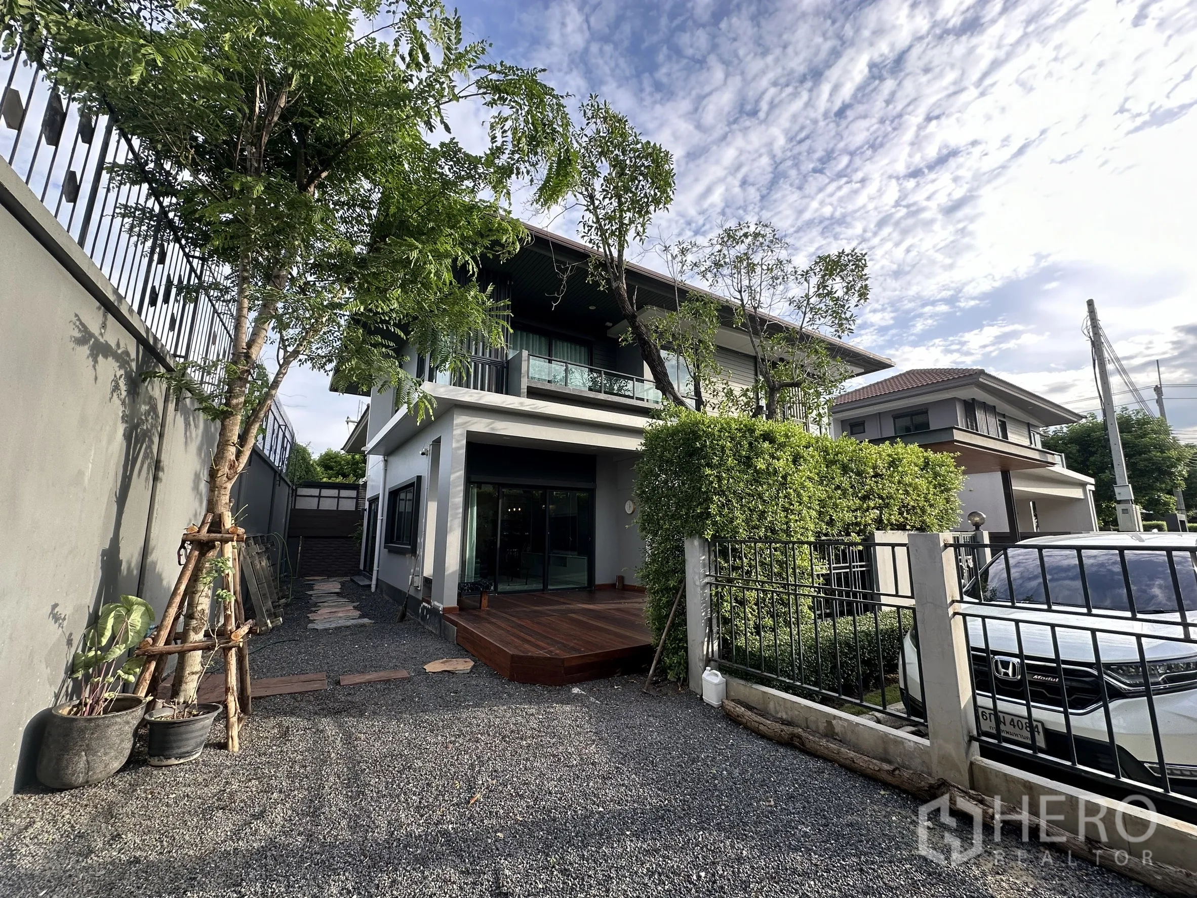 Detached House for rent or sale in Lam Luk Ka, Pathum Thani - Front yard and driveway with trees, metal fence and gravel leading to the house façade.