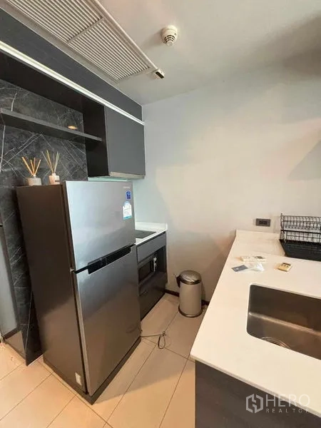 Condominium for rent or sale in Watthana, Bangkok - Modern kitchenette with stone countertop, stainless sink and full-size refrigerator.