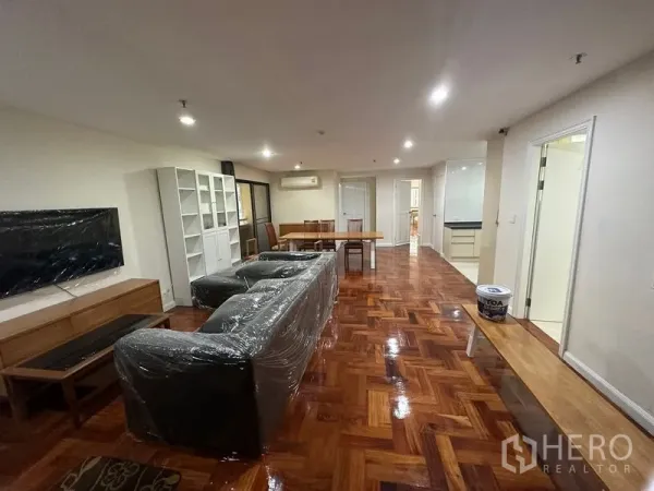 Condominium for rent in Watthana, Bangkok - Open-plan living and dining area with sofa, TV wall, shelving units, and shiny parquet flooring.