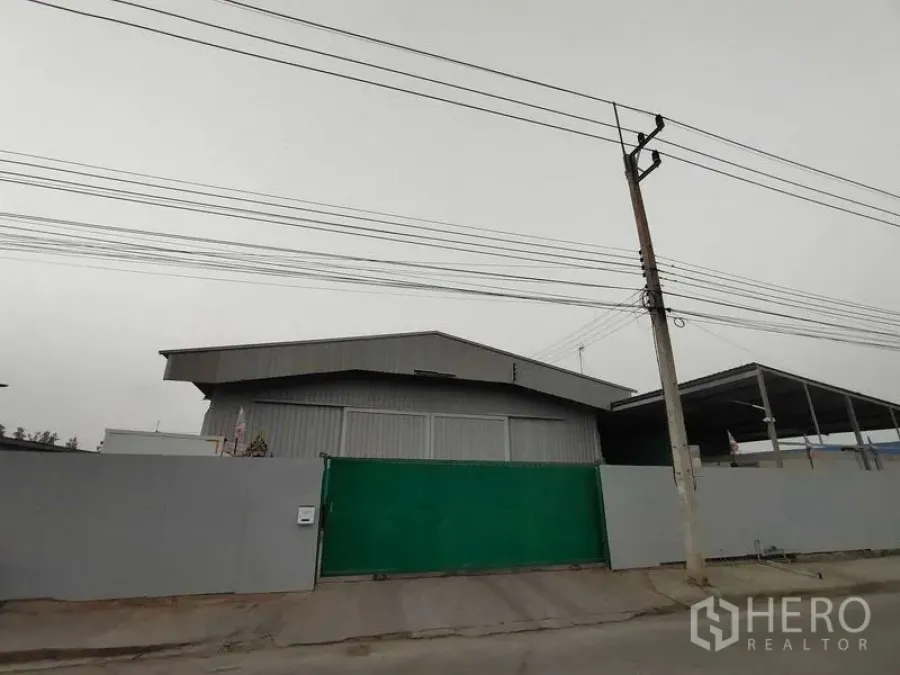 คลังสินค้า ขายในLam Luk Ka, Pathum Thani - มุมมองด้านหน้าของโกดังพร้อมรั้วโลหะและประตูสีเขียวจากถนน