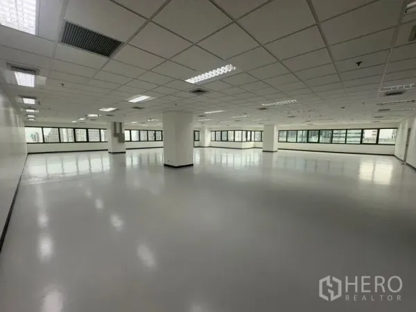 Office Space for rent in Bang Rak, Bangkok - Corner office space with wraparound windows, structural columns, and suspended ceiling lights allowing abundant daylight.