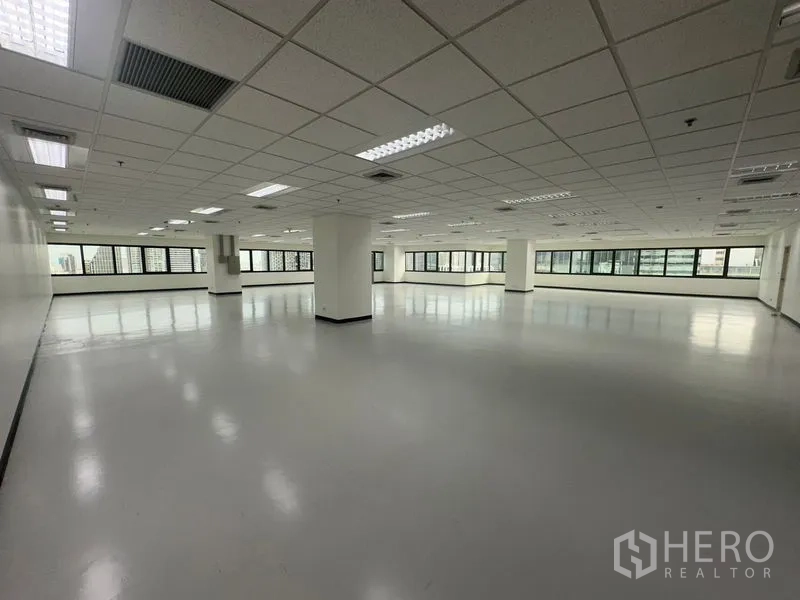 Office Space for rent in Bang Rak, Bangkok - Corner office space with wraparound windows, structural columns, and suspended ceiling lights allowing abundant daylight.