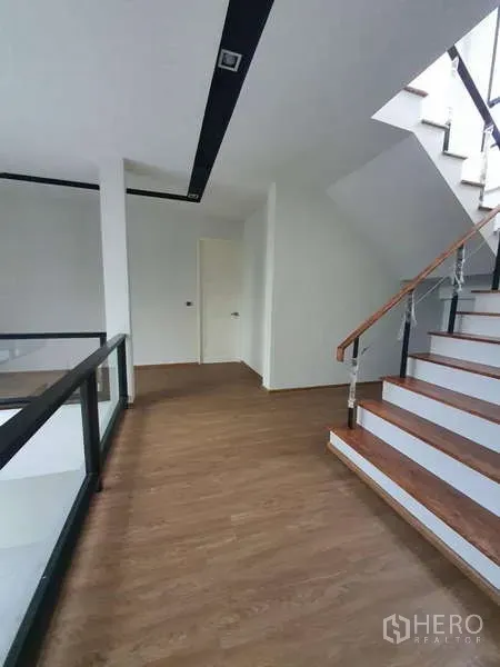 Detached House for rent in Phra Khanong, Bangkok - Staircase with wooden steps and glass railing leading to the upper landing.