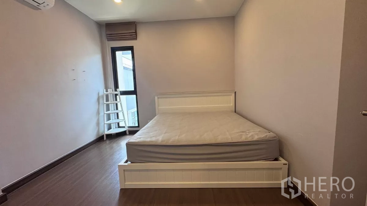 Detached House for rent or sale in Saphan Sung, Bangkok - Spacious bedroom with white bed frame, tall window and door to a small balcony on wood floors.
