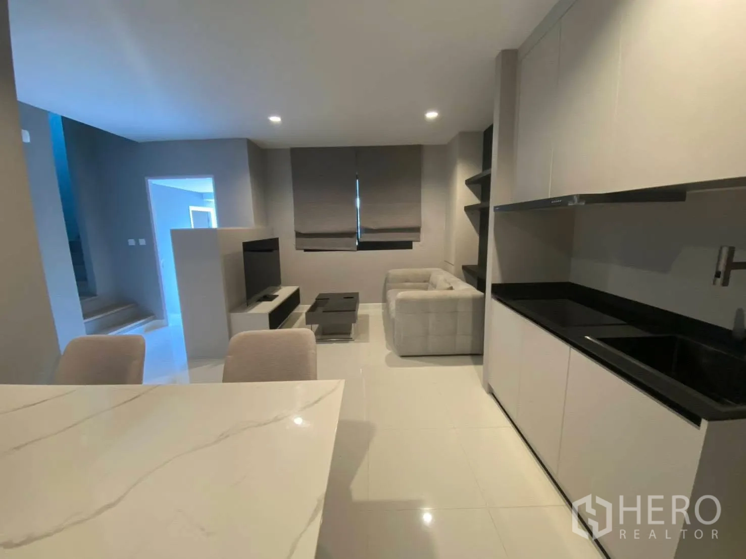 Townhouse for rent in Bang Kapi, Bangkok - Open-plan kitchen with black countertops facing a cozy living area with sofa and TV unit.