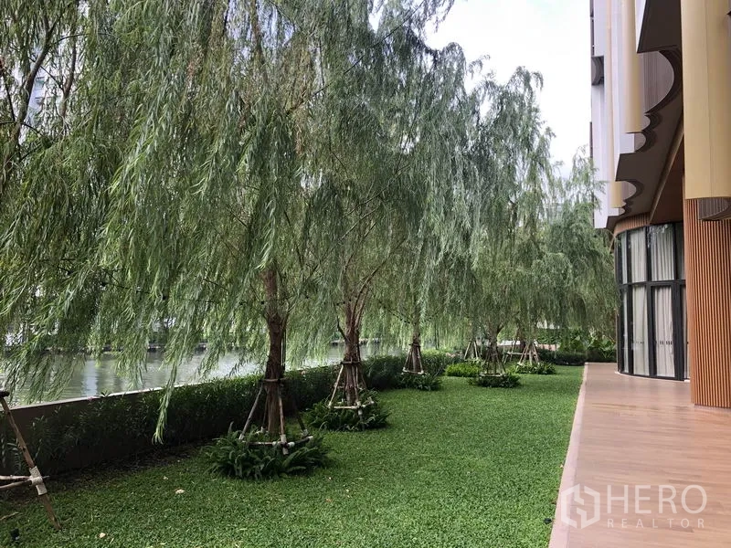 Condominium for sale in Watthana, Bangkok - Riverside lawn lined with willow trees beside the condominium.