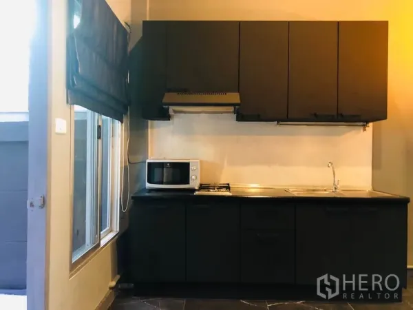 Townhouse for rent in Bang Kapi, Bangkok - Compact modern kitchen with black cabinetry, gas hob, hood, sink and a window.