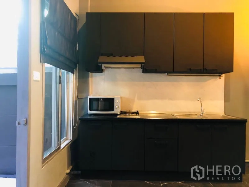 Townhouse for rent in Bang Kapi, Bangkok - Compact modern kitchen with black cabinetry, gas hob, hood, sink and a window.