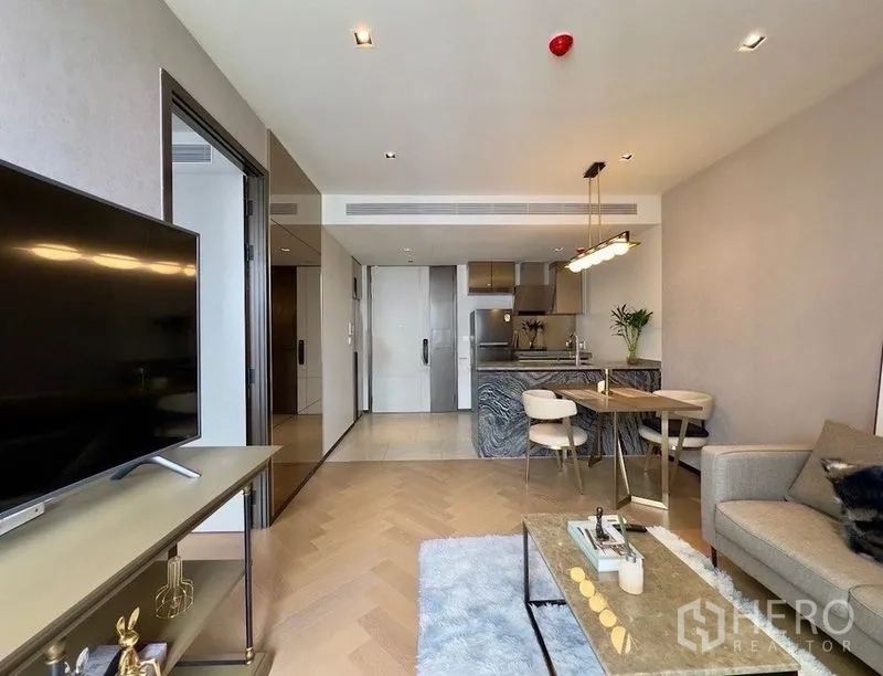 Condominium for rent or sale in Watthana, Bangkok - Living area with TV console, rug, and view toward the kitchen and dining counter.