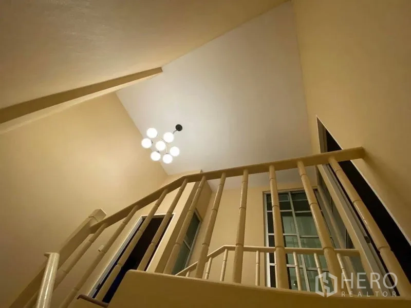 Townhouse for rent in Lat Phrao, Bangkok - Stairwell view with modern pendant light and cream walls creating a bright landing.