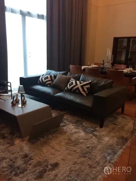 Condominium for rent in Khlong Toei, Bangkok - Contemporary living room featuring a leather sofa, plush rug, and modern coffee table beside the dining area.